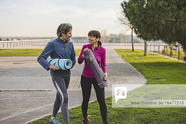 Happy mature couple walking with exercise mats in park