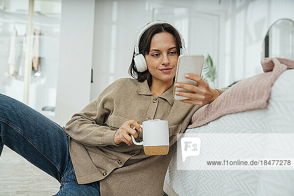 Lächelnde junge Frau mit Kaffeetasse und Mobiltelefon