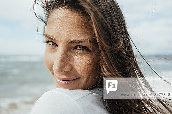 Lächelnde Frau mit langen braunen Haaren am Strand