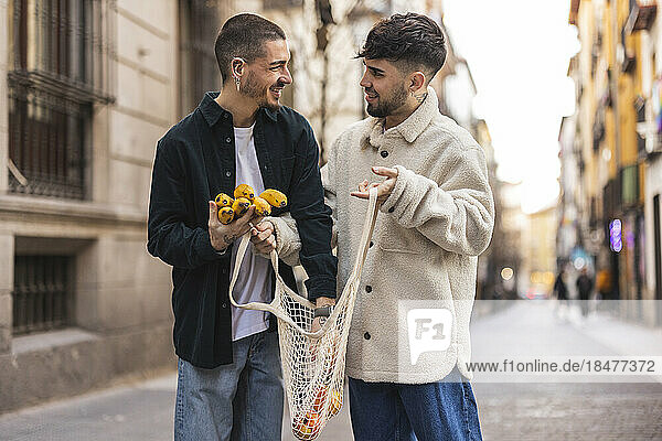 Happy gay man with boyfriend putting banana in mesh bag at street