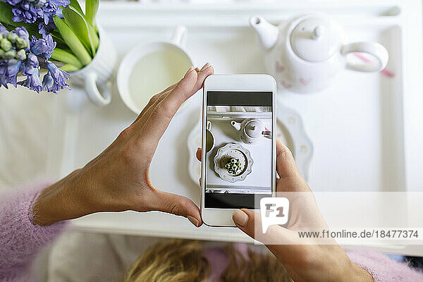 Frau fotografiert Cupcake mit Smartphone zu Hause im Bett