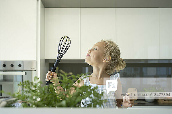 Girl holding egg beater in kitchen at home