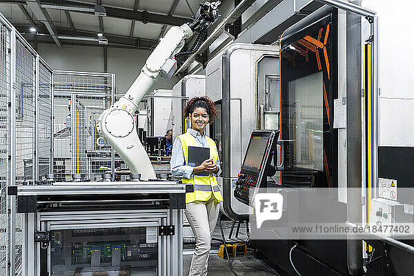 Smiling engineer standing with tablet computer by machine in factory