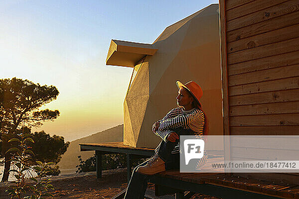 Young woman sitting near sustainable building on sunset