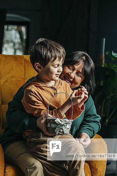 Glückliche Großmutter mit Enkel  der auf einem Sessel Ostereier aus Schokolade hält