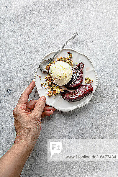 Woman's hand holding plate of pears in red wine with ice cream and granola