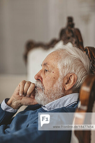 Contemplative senior man sitting on chair at home