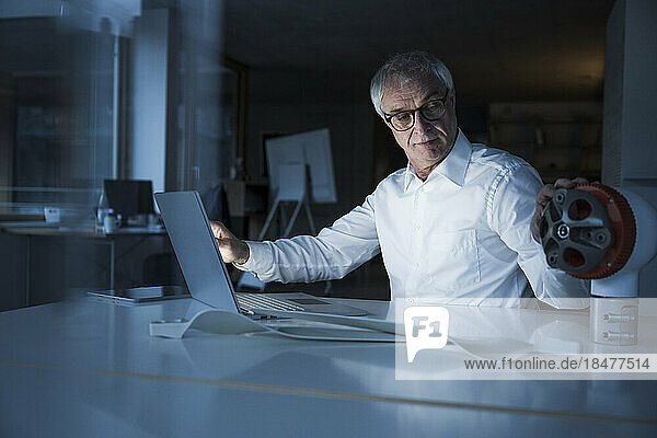 Senior engineer examining rotor sitting with laptop at desk in office