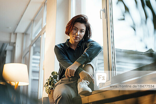 Young businesswoman with short hair sitting on window sill