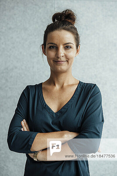 Smiling businesswoman with arms crossed in front of wall