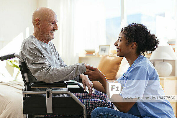 Happy physical therapist holding hand of senior man sitting on wheelchair
