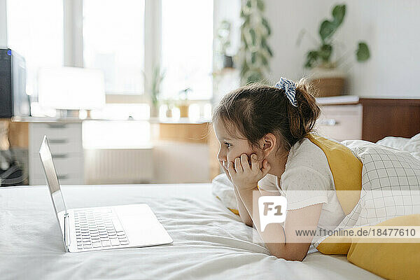 Mädchen beobachtet Laptop  der zu Hause auf dem Bett im Schlafzimmer liegt