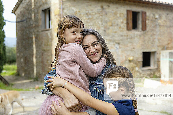 Happy mother embracing daughters in front of house