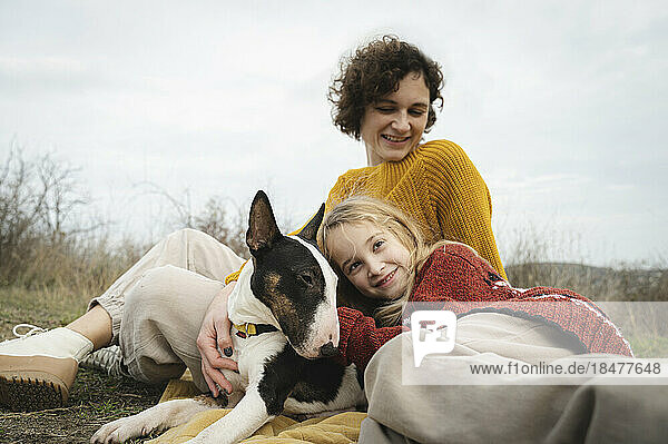 Daughter and mother relaxing with dog in front of sky