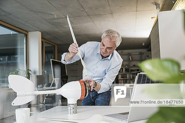 Elderly businessman installing blade on wind turbine rotor