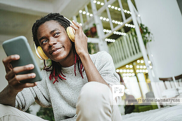 Thoughtful young man listening to music through headphones at home