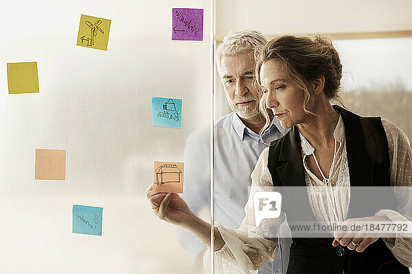 Businesswoman with businessman discussing over adhesive notes at office