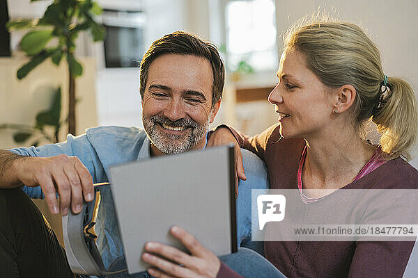 Lächelnder Mann schaut auf Tablet-PC  der von einer Frau zu Hause gehalten wird