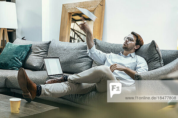 Businessman playing with paper airplane on sofa at office