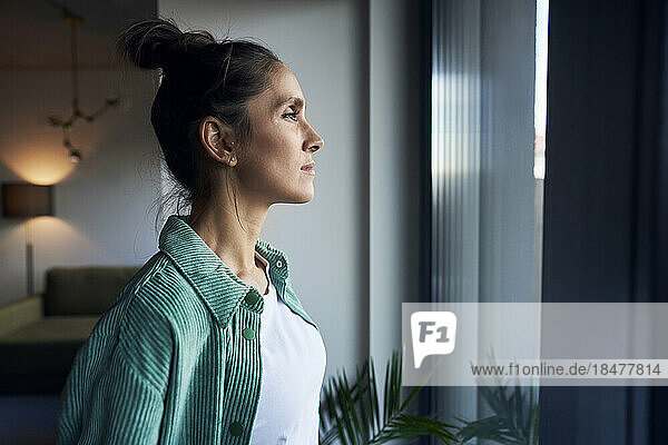 Thoughtful woman standing in front of window at home