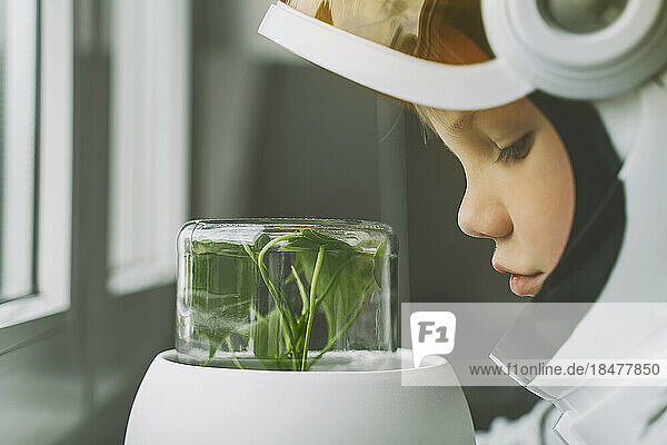 Boy wearing space suit looking at plant in glass jar