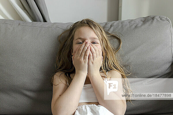 Girl covering face sitting on sofa at home