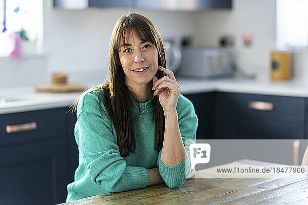Smiling woman sitting at table in kitchen at home