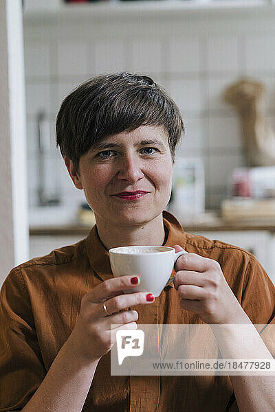 Smiling mature woman holding coffee cup at home