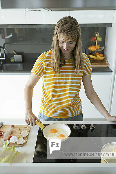 Smiling woman making fried eggs in kitchen at home