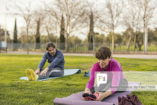 Smiling woman with man doing yoga in park