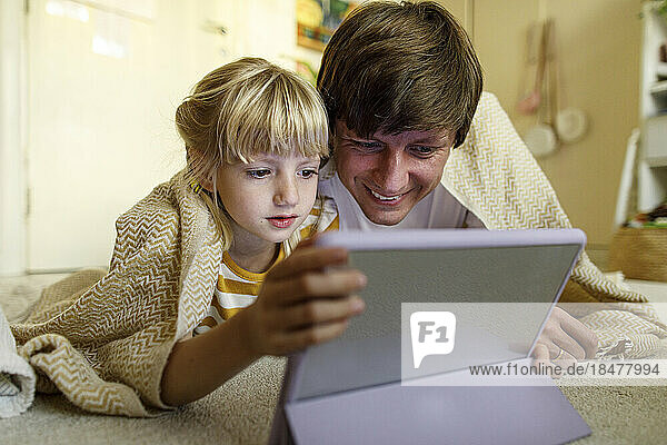 Father and daughter watching tablet PC lying on floor at home