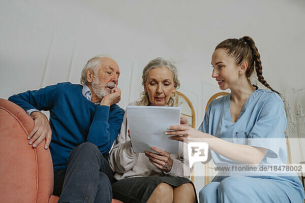 Smiling nurse assisting senior man and woman reading medical reports at home