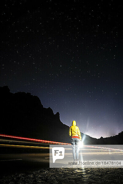 Spanien  Kanarische Inseln  Fahrzeuglichtspuren fahren an einer Frau vorbei  die am Straßenrand im Nationalpark El Teide steht