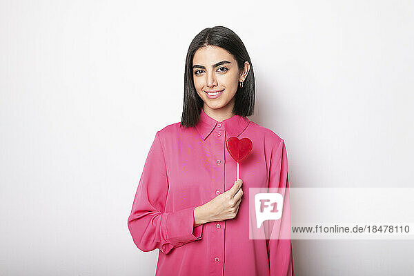 Happy woman standing with red heart shaped lollipop