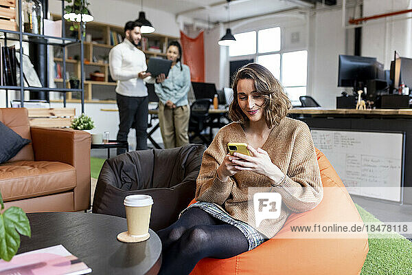 Smiling businesswoman using mobile phone sitting on bean bag in office