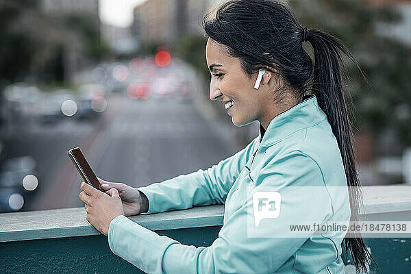 Smiling woman wearing in-ear headphones using smart phone