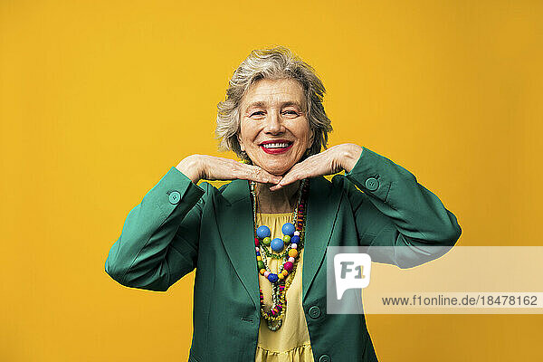 Happy senior woman standing against yellow background