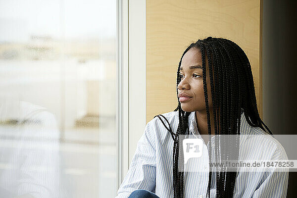 Thoughtful young woman with braided hair looking out of window