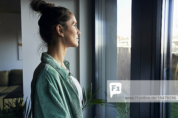 Contemplative woman standing looking through window at home
