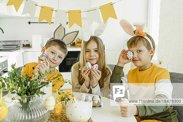 Glückliche Jungen und Mädchen tragen Hasenohren-Stirnbänder und halten Ostereier zu Hause