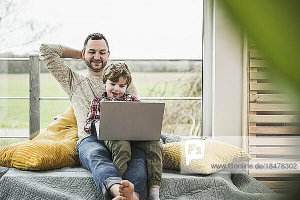 Smiling father and son watching laptop together at home