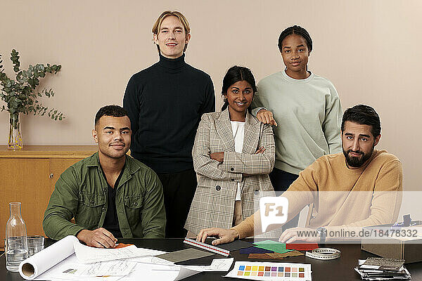 Confident multiracial fashion designers at desk in studio