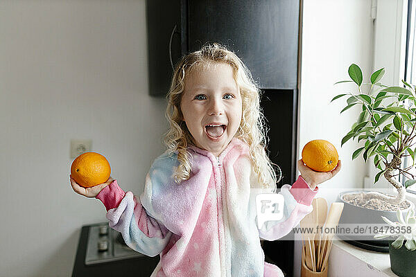 Glückliches Mädchen hält Orangen in der heimischen Küche