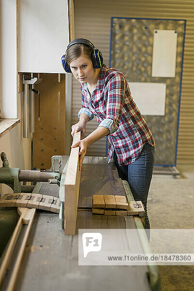 Craftswoman wearing ear protectors cutting wood in workshop