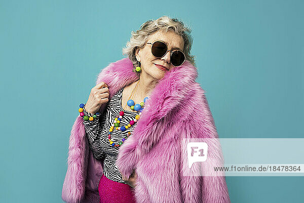 Cool senior woman wearing pink fur coat against colored background
