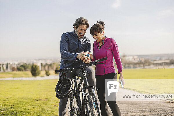 Glückliches älteres Paar mit Fahrrad und Smartphone im Park