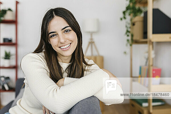 Happy young woman sitting on sofa at home