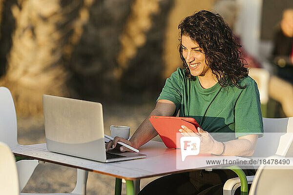 Happy woman using laptop sitting at outdoor cafe