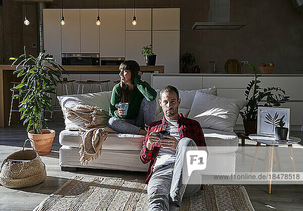 Mann und Frau sitzen mit Getränken im Wohnzimmer zu Hause
