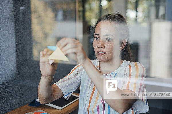 Young businesswoman sticking adhesive notes on soundproof glass in office